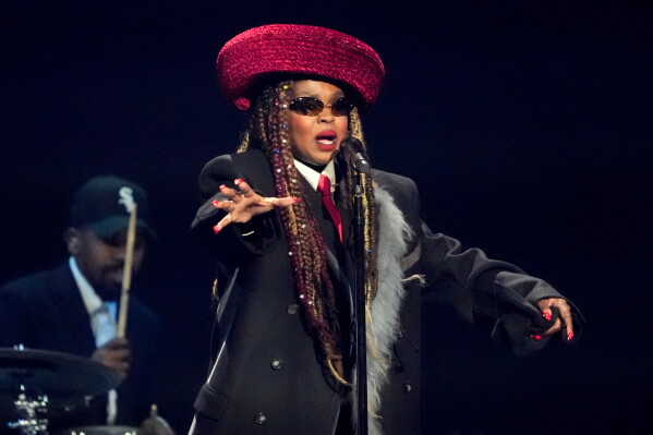 Lauryn Hill se apresenta no palco usando chapéu vermelho e traje preto