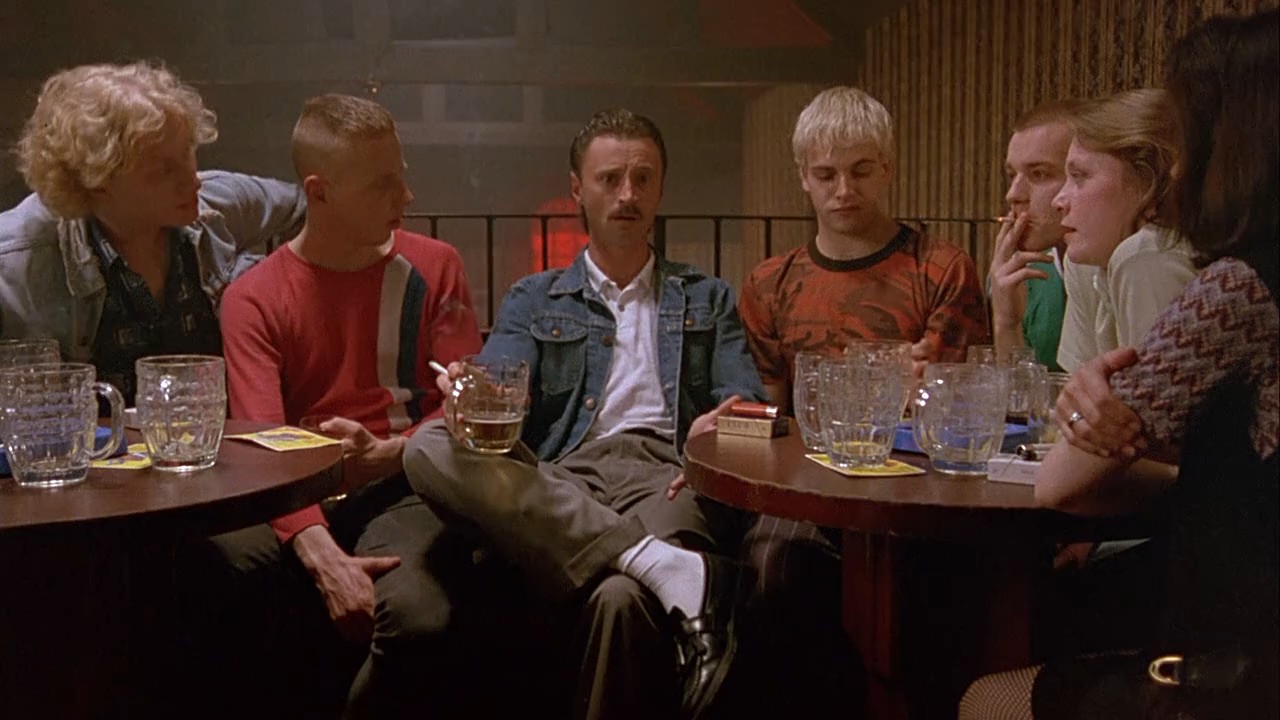 Renton e seus amigos sentados em um pub em uma cena de Trainspotting.