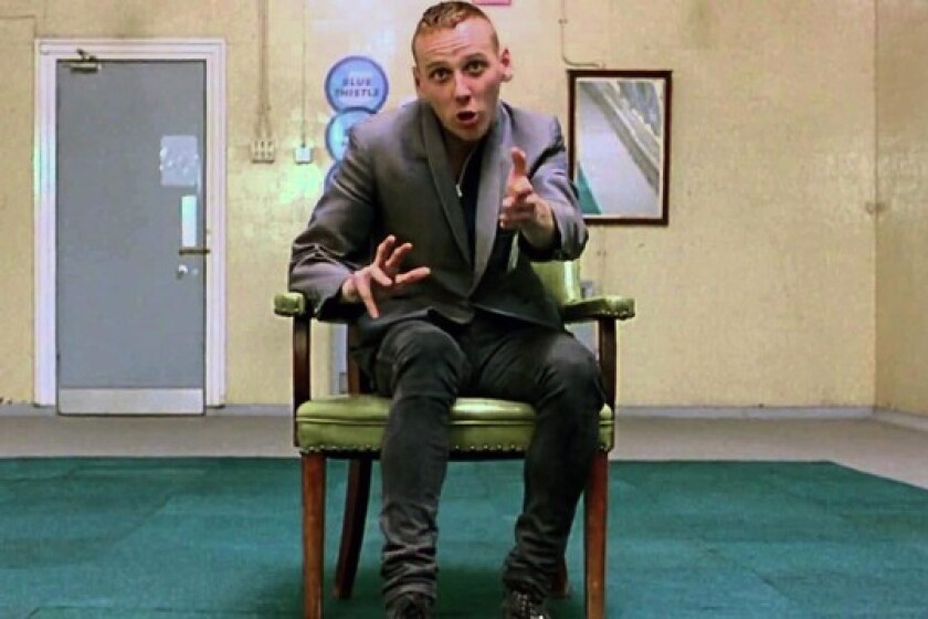 Spud, interpretado por Ewen Bremner, sentado em uma entrevista de emprego em Trainspotting.